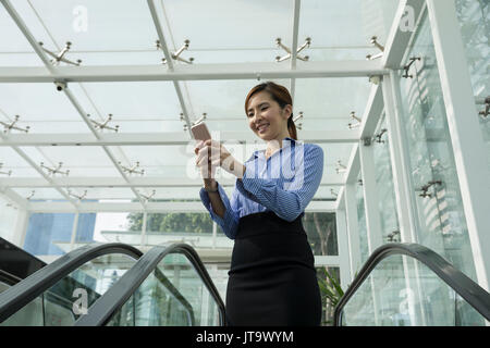 Chinese businesswoman using her Smart phone on an escalator. Stock Photo