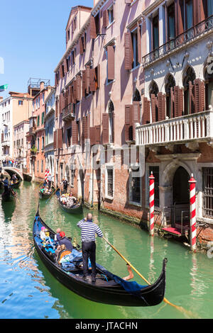 Gondolier, rowing a gondola, with tourists, along canal, in front of a palazzo, Venice, UNESCO, Veneto, Italy, Europe Stock Photo