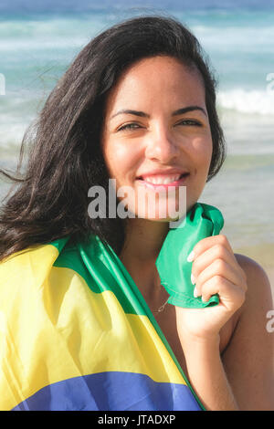 Young Brazilian woman, 20 to 29 years old, wrapped in the Brazilian flag on a beach in Rio de Janeiro, Brazil Stock Photo