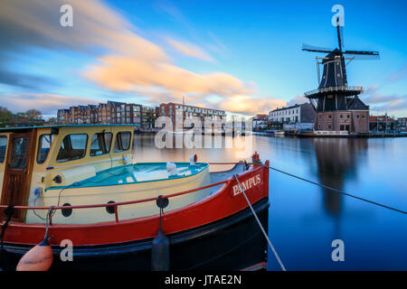The fishing boat frames the Windmill De Adriaan reflected in the River Spaarne at dusk, Haarlem, North Holland, The Netherlands Stock Photo