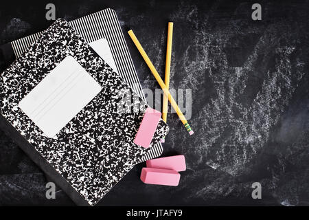 Back to school supplies. Books, erasers and pencils over a chalkboard or blackboard with room for copy space. Stock Photo