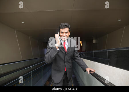 Indian business Man using his Smart phone while standing on an escalator in the city. Stock Photo