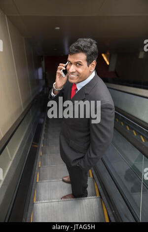 Indian business Man using his Smart phone while standing on an escalator in the city. Stock Photo