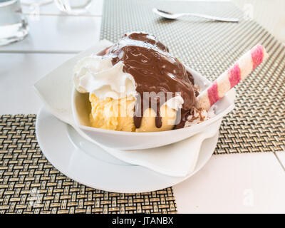 Vanilla ice cream dessert with cream and chocolate and a tube wafer with a pink twirl, served in a white triangular dish. Stock Photo