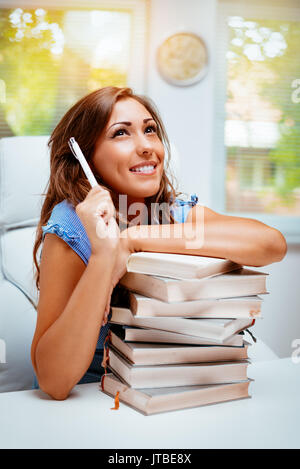 Beautiful teenage girl sitting in library with books and thinking. Stock Photo