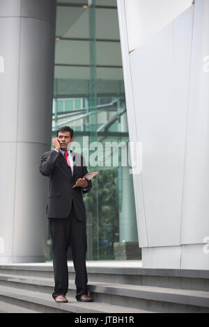 Indian businessman talking on his Smart phone outdoors in Asian city. Stock Photo