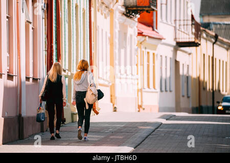 Grodno, Belarus - June 11, 2017: Two Young Women Walking Near Facades Of Old Traditional Houses Buildings In Sunny Summer Day In Hrodna, Belarus Stock Photo