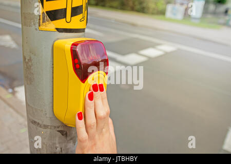 Woman's hand on a yellow walk button near the street, yellow walk button on a pole touched by woman's hand Stock Photo