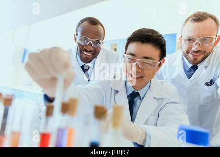 Group of smiling scientists in protective eyeglasses working together in chemical laboratory Stock Photo