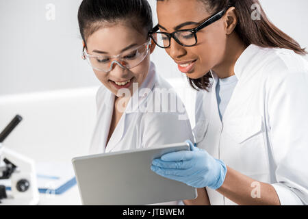 Smiling young scientists in eyeglasses using digital tablet in laboratory, scientists working together Stock Photo