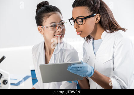 Smiling young scientists in eyeglasses using digital tablet in laboratory, scientists working together Stock Photo