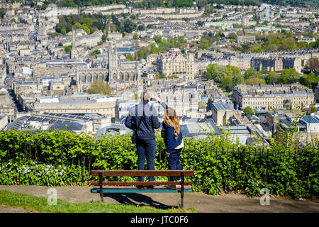 A man and a woman are pictured looking down from Alexandra Park and taking a photograph of a scenic view of the city of Bath and Bath Abbey Stock Photo