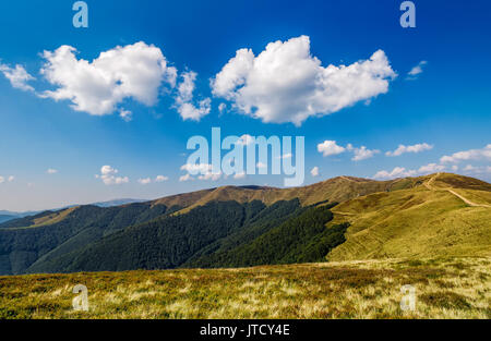 beautiful clouds on a blue sky over mountain ridge with grassy meadows and green forests Stock Photo