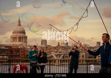 Street artist creating bubbles with soap in front of the Tate Modern museum in London South Bank, with St.Paul's Cathedral in the background. Stock Photo