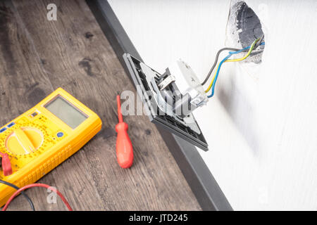 Electrician a wall socket with electronic multimeter Stock Photo