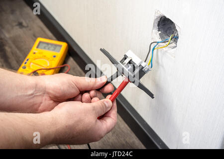 Electrician a wall socket with electronic multimeter Stock Photo