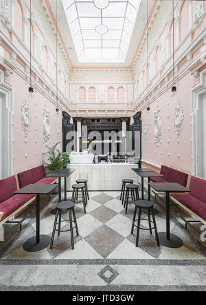 Coffee zone in the antique restaurant with white stucco molding on the pink walls and large window on the ceiling. There are red sofas, tiled rack wit Stock Photo