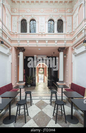 Antique restaurant with white stucco molding on the pink walls and a tiled floor. There are red sofas, black tables and stools, columns, arch entrance Stock Photo
