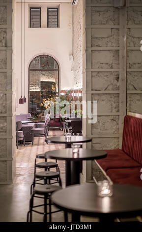 Cafe in a loft style with luminous lamps and shabby walls with wooden panel. There are multicolored sofas, different tables, stools and chairs, plants Stock Photo