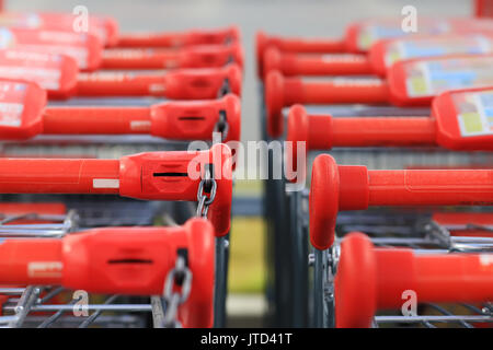 Red handles of shopping trolleys standing in row. Shopping trolley handles close-up. Stock Photo