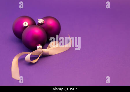 Beautiful purple christmas balls with satin effect and grey gift ribbon on purple background. Stock Photo