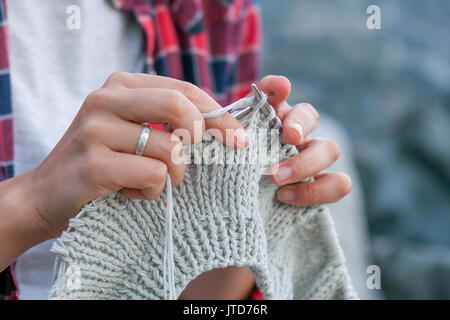 Close-up Young woman checkered red shirt and white t-shirt knits with knitting needles gray sweater from natural woolen threads, in the background sto Stock Photo
