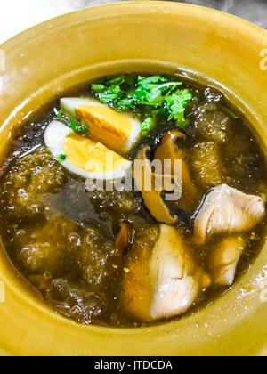 Fish maw soup with meat, egg and vegetable in earthen bowl (Braised Fish Maw in red gravy), Asian Thai Chinese street food. Stock Photo