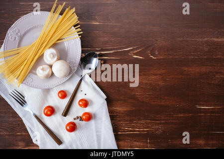 Ingredients for pasta on a wooden table. Plate, cutlery, pasta and fresh vegetables top view Stock Photo