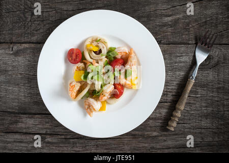 Salad with squid rings, shrimps, pepper and tomatoes on a white plate Stock Photo