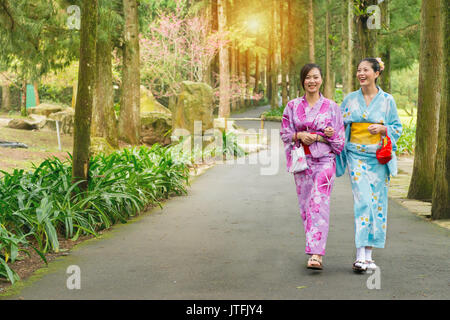 beautiful girlfriends traveler women wearing japanese kimono clothing together and walking on tree path in japan cherry blossoming sakura park at sunl Stock Photo