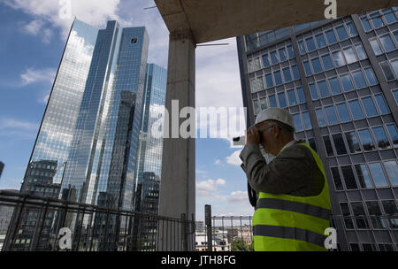 A man takes a photograph of the headquarters of the Deutsche Bank (German Bank) from the Marienforum in Frankfurt am Main, Germany, 9 August 2017. The building is one of several new office complexes currently under construction in the Central Banking District of the city. Photo: Boris Roessler/dpa Stock Photo