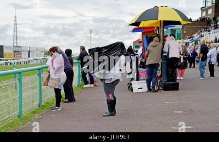 Brighton, UK. 9th Aug, 2017. This racegoer has trouble with her coat in the wind and rain at the Marstons Race Day in the Maronthonbet Festival of Racing at Brighton Racecourse Credit: Simon Dack/Alamy Live News Stock Photo