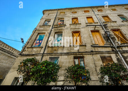 Old building in downtown Avignon France with boarded up windows and very colorfully painted scenes on the windows Stock Photo