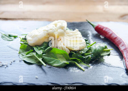 White fish fillet with herbs and chili on fried spinach. Gray background. Stock Photo