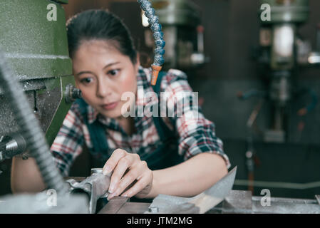 professional milling machining female employee put steel parts into automatic machine and drilling in factory processing working space. selective focu Stock Photo