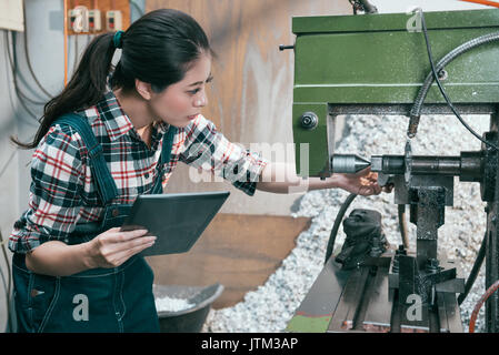 attractive pretty lathe worker manager holding mobile pad computer to checking working process and adjusting milling machine confirm product. Stock Photo