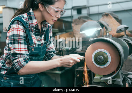 beauty pretty female lathe company employee wearing safety goggles to grind steel product and using abrasive disc machine working. Stock Photo