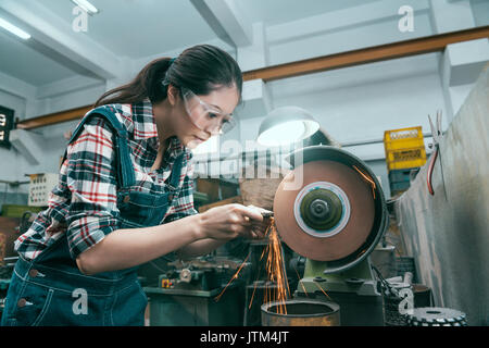 young beautiful milling machining worker using abrasive wheel tool grinding metal components . Stock Photo