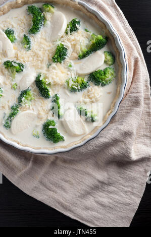 Broccoli  pie on dark wooden table and light towel. Cooking process. Not baked Stock Photo