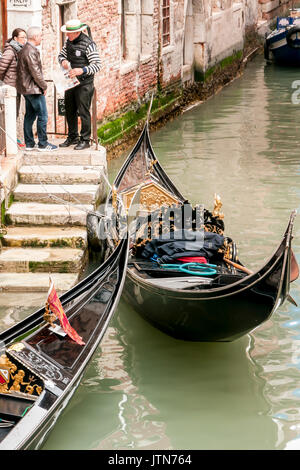 Two Gondoliers by their Gondolas by steps  in a Venetian canal. Stock Photo