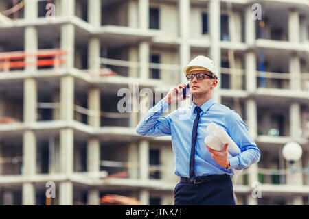 Construction engineer at the construction site looking at the camera and talking mobilephone Stock Photo