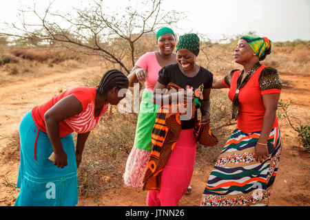 Mforo, Tanzania a village near Moshi, Tanzania. Solar Sister Entrepreneurs visit and have fun after their Solar Sister business meeting at Fatma Mzirayâs house. Fatma Mziray, dressed in a red top and a patterned scarf, Mwunaidi Msuya - Solar Sister Entrepreneur, dressed in a green scarf and pink top, Grace Mbwambo - Solar Sister Entrepreneur, dressed in a red top and turquoise skirt, Grace Kimaro - Solar Sister Entrepreneur in white top and scarf, and Sadia Abdallah - Solar Sister Entrepreneur, dressed in a black scarf and a black top with a design. Stock Photo