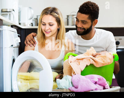 Afro husband and white housewife using washing machine in home interior Stock Photo