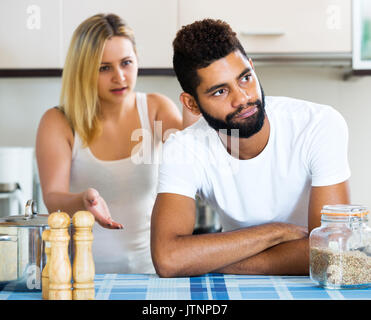 Sad young man and white crying woman fighting in domestic kitchen. Focus on the man Stock Photo