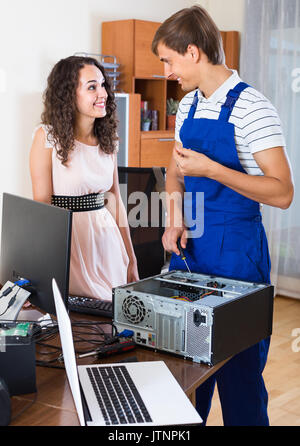 Portrait of happy female and PC repairman fixing computer. Focus on man Stock Photo