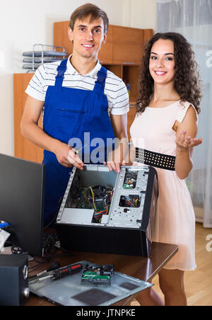 Portrait of smiling young woman and PC repairman fixing computer indoors Stock Photo