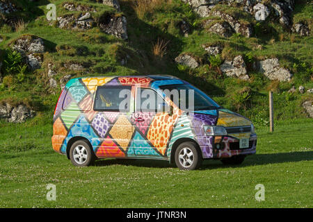 Rainbow coloured geometric design on exterior of campervan parked on green grass beside rocky hill in Scotland Stock Photo