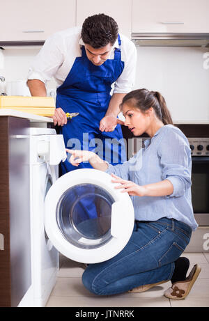 Young housewife and repairman near broken washing machine at home kitchen Stock Photo
