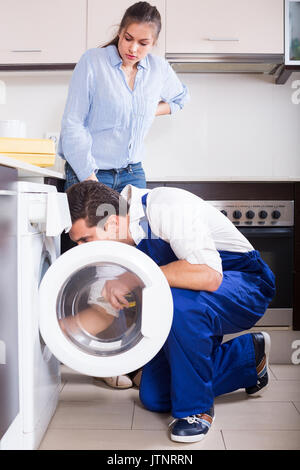 Young woman and professional mechanic repairing broken washing machine at home kitchen Stock Photo