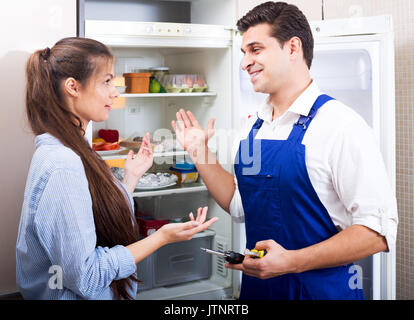 Young  housewife and cheerful handyman with tooling standing near fridge indoors Stock Photo